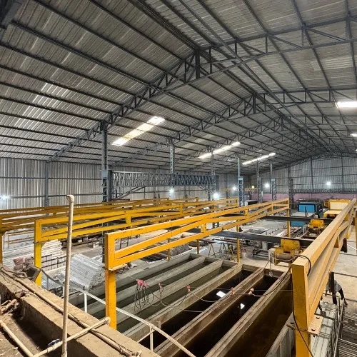 The wide shed: a yellow overhead gantry crane running the length of long treatment tanks below, with steel roof trusses and cladding above and the bay stretching into the distance.