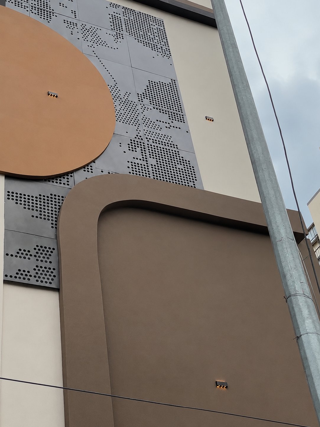 Perforated Panel: a façade combining grey perforated metal screens with warm corten-toned panels.