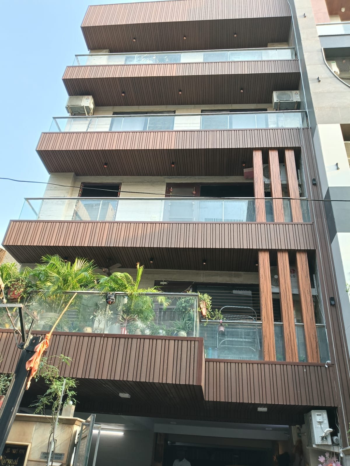 Looking up the front of a residence: every balcony fascia and soffit is clad in fine vertical composite battens in a deep brown, floor after floor, with wider rafter posts in a lighter grain running down the right-hand bay between the glass balustrades.